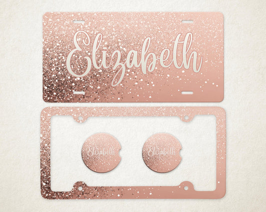 May include: Rose gold glitter license plate and frame set with the name "Elizabeth" in a white script font. The set includes two matching car coasters. The license plate and frame have a sparkly, glittery appearance.