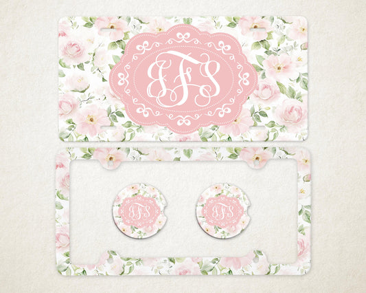 May include: A license plate and car accessories set featuring a floral design with pink roses and green leaves. The set includes a license plate, a license plate frame, and two car coasters. Each item has a pink oval with white initials.