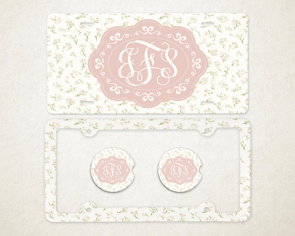 May include: A license plate, license plate frame, and two car coasters with a floral pattern. The license plate and coasters have a pink oval with the letters "JFS" in a white script. The license plate frame is clear.