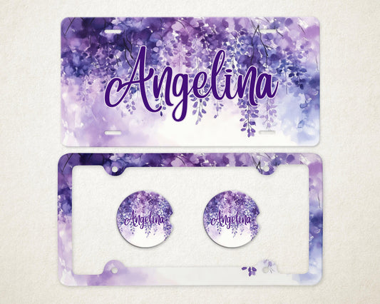 May include: A license plate and car accessories set featuring a watercolor floral design in shades of purple and white. The name "Angelina" is written in a cursive font. Includes a license plate, license plate frame, and two car coasters.
