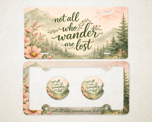 May include: License plate and car coasters set with a watercolor design. The license plate and coasters feature the text "not all who wander are lost" with a scenic mountain and floral background.