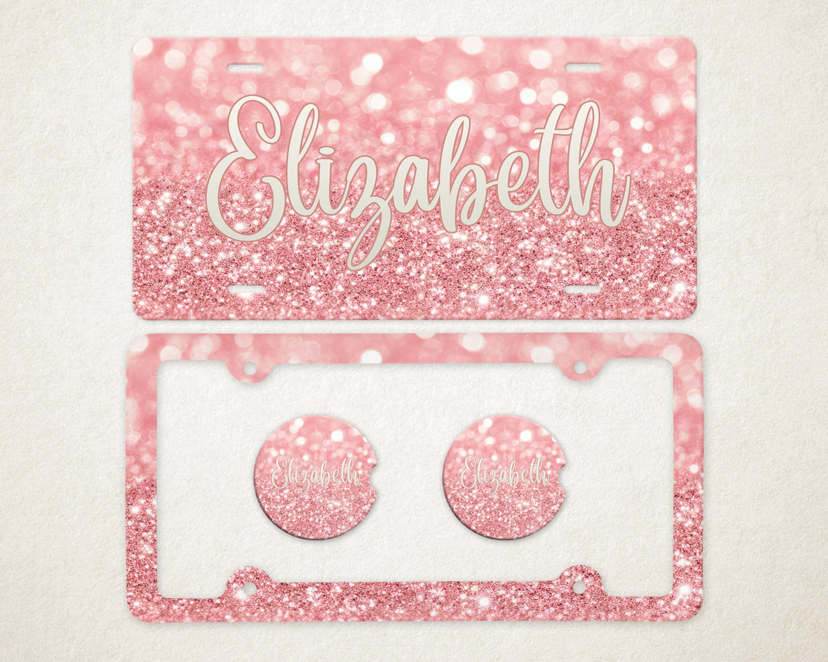 May include: A pink glitter license plate and car accessories set. The license plate has the name "Elizabeth" in a cursive font. The set includes a license plate frame and two car coasters, all with a matching glitter design.