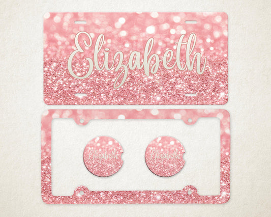 May include: A pink glitter license plate and car accessories set. The license plate has the name "Elizabeth" in a cursive font. The set includes a license plate frame and two car coasters, all with a matching glitter design.
