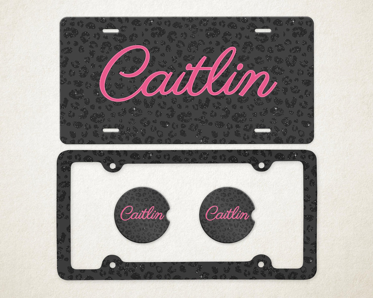 May include: A license plate and car coasters set. The license plate and coasters have a black leopard print design with the name "Caitlin" in pink script. The license plate frame is black.