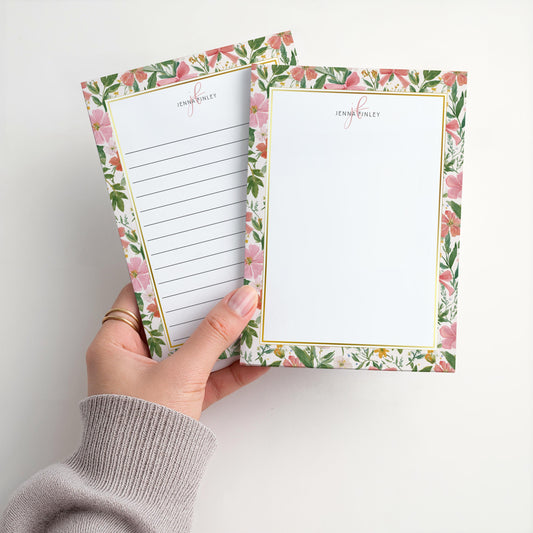 May include: Two floral notepads with a gold border and the name "Jenna Finley" printed at the top. One notepad has lined paper, and the other is blank. The floral design features pink flowers and green leaves.
